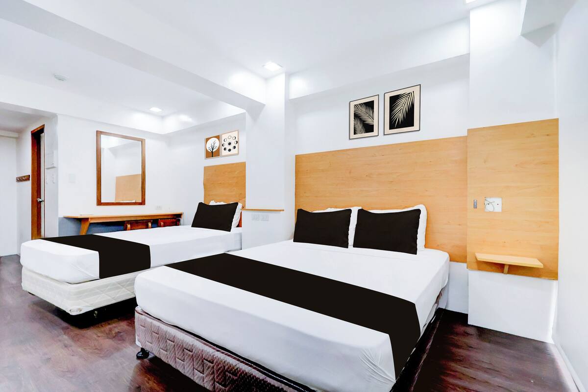 Habitació d'hotel amb dos llits, ambres de fusta, un escriptori petit i un mirall.