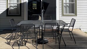 A patio with a table and chairs, a large umbrella, and a house with a gabled roof and windows. - Modern Cabin Higgins Lake; walk to Hiking, XC Ski, River, Town, near golf + ORV (Roscommon)