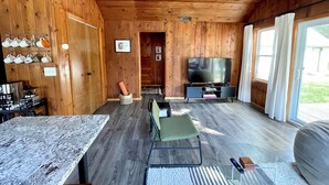 A wooden-paneled room with a TV, seating area, and a table with a marble top. - Modern Cabin Higgins Lake; walk to Hiking, XC Ski, River, Town, near golf + ORV (Roscommon)