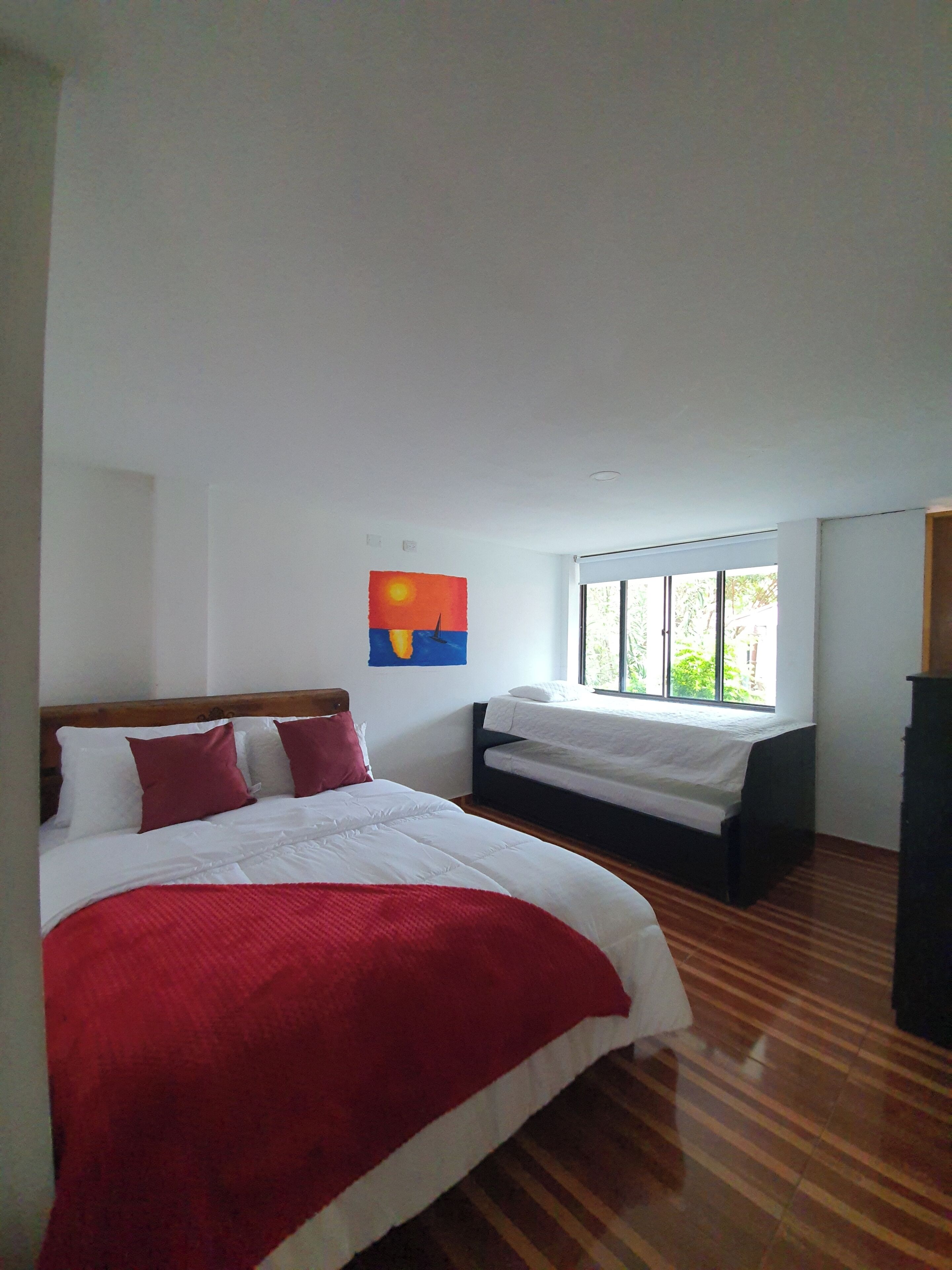 A bedroom with a large bed, a smaller bed, and a window with a view of greenery.