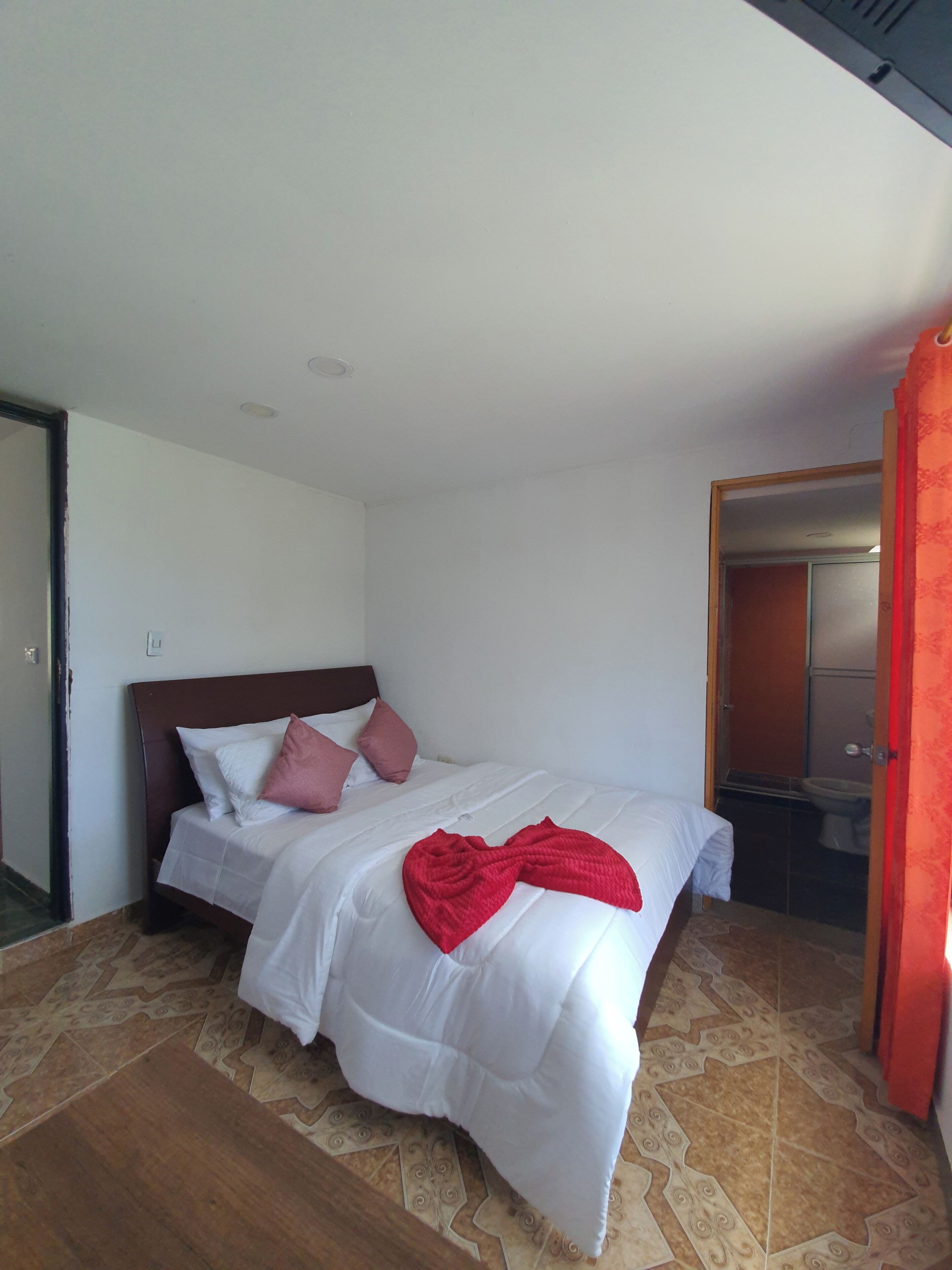 A bedroom with a bed, a wooden headboard, and a red blanket.