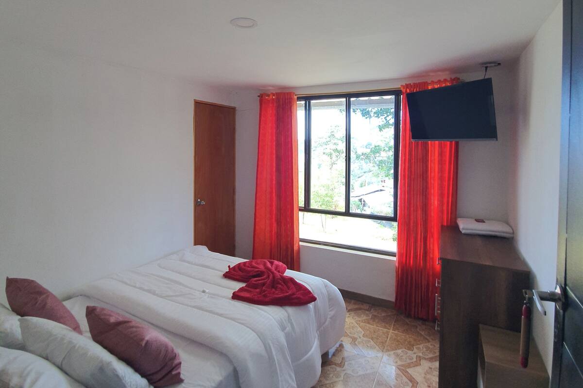 A hotel room with a bed, a desk, a TV, and a window with curtains.