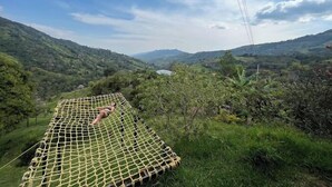 Una hamaca colgando entre árboles en un valle exuberante, con vistas a colinas distantes.