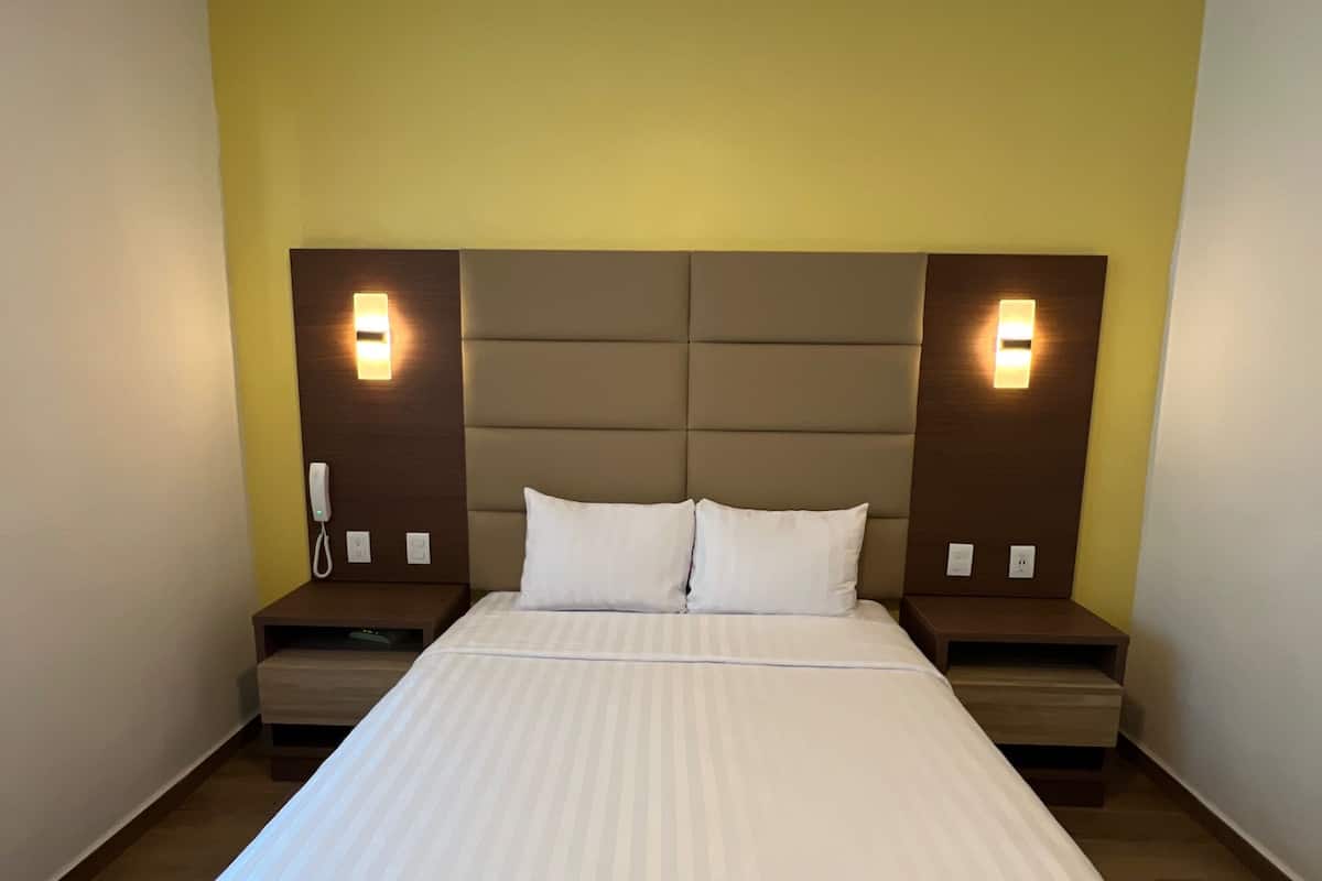 Habitación de hotel con una cama grande, dos mesitas de noche y cabecera con iluminación integrada.