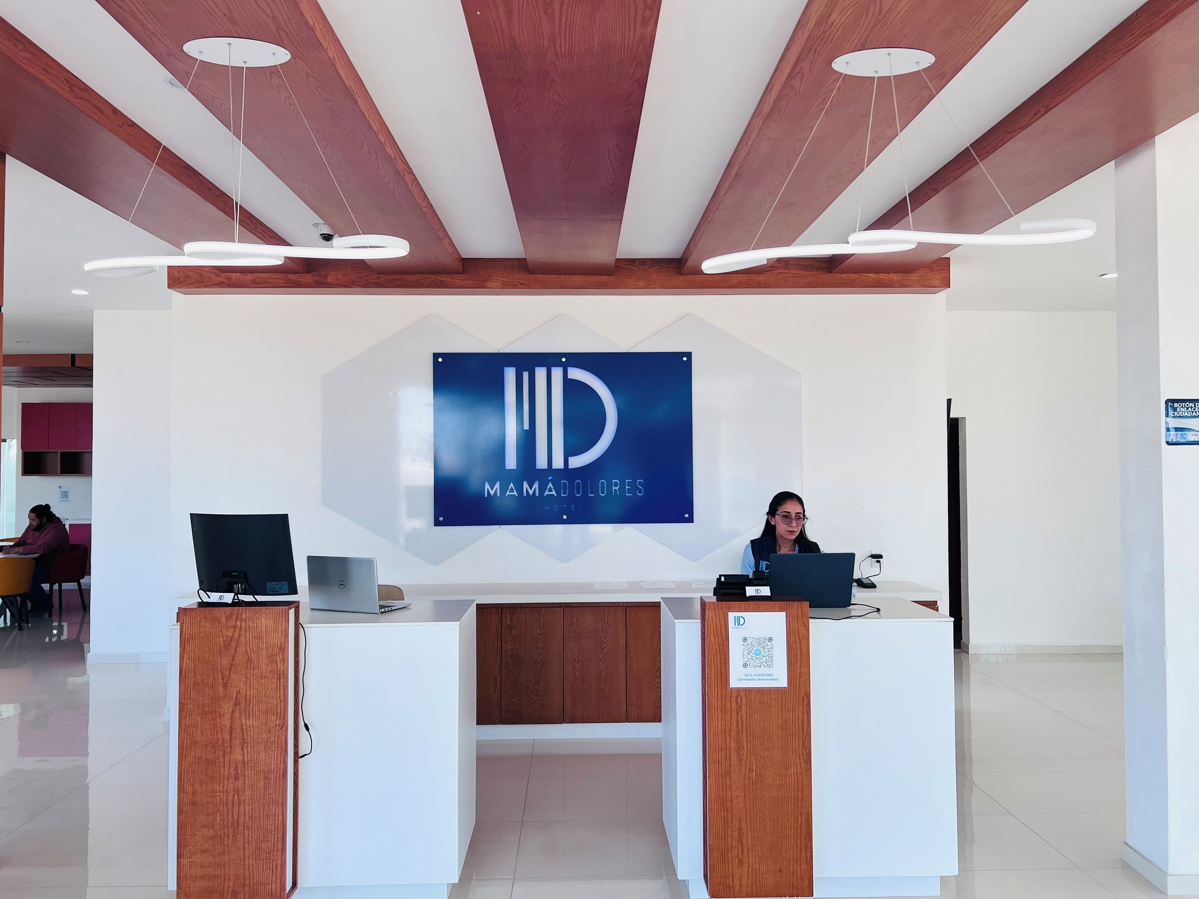 Un mostrador de recepción con un logotipo, dos monitores de ordenador y un código QR para ID Mamadóres Hotel.