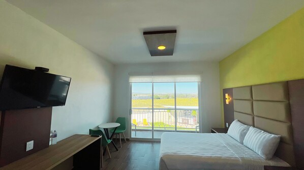 Une chambre d’hôtel équipée d’un lit, d’un bureau, d’une chaise, d’une télévision et d’une grande fenêtre donnant sur l’extérieur.