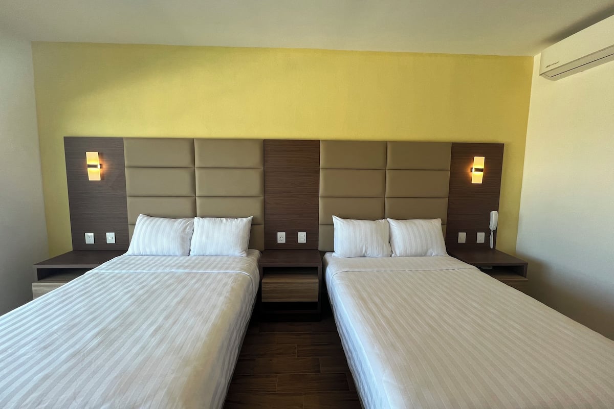 Una habitación de hotel con dos camas, un cabecero de madera y lámparas de noche.
