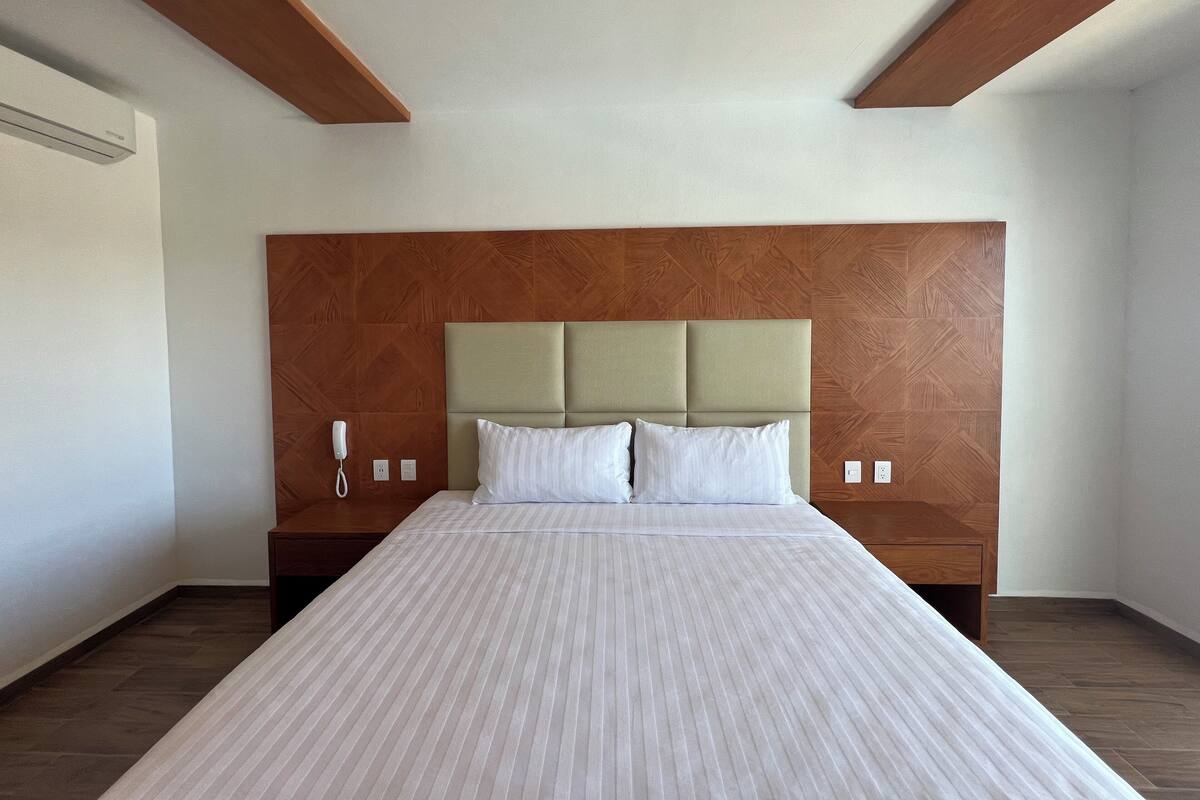 Habitación de hotel con una cama grande, cabecero de madera y un teléfono en la mesita de noche.