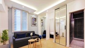 Un salon moderne avec un canapé, une table basse et une plante en pot. Une porte-fenêtre coulissante donne accès à une salle de bain avec douche.