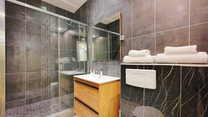 Une salle de bain moderne avec une douche à parois de verre, un meuble-lavabo en bois et un mur recouvert de carreaux de marbre.