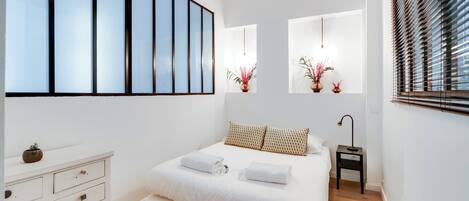 A modern bedroom with a large bed, a dresser, and a bedside table with a lamp.