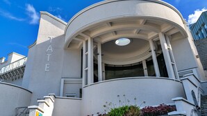 A building with a curved facade, a prominent entrance with a circular skylight, and the word "GALLERY" visible on the side. - No. 6 Porthgwidden (St Ives)