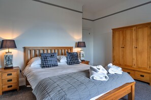 Una cama bien hecha con una colcha gris acolchada, dos lámparas de noche y un armario de madera.