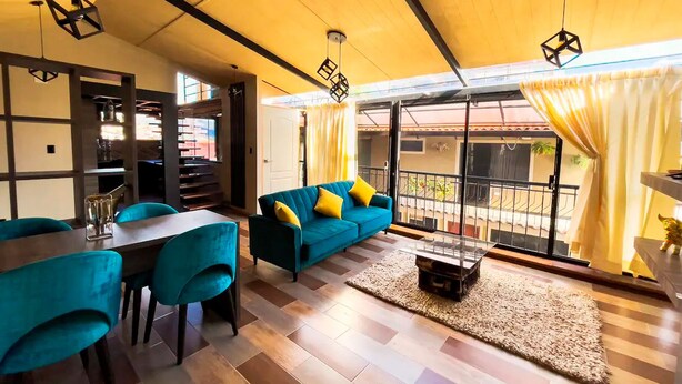 A modern living room with a sofa, chairs, and a dining table. There is a balcony with yellow curtains and a view of the outside. - L'Aurora Residencial Cusco (Cusco)