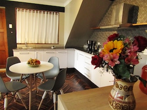 A compact kitchen with white cabinets, a dining area with a round table and chairs, and a vase with flowers on the table.