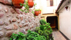 A narrow alleyway with a stone wall, potted plants, and a building entrance. - L'Aurora Residencial Cusco (Cusco)