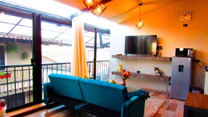 A living room with a blue sofa, a TV mounted on the wall, and a balcony with a railing. - L'Aurora Residencial Cusco (Cusco)