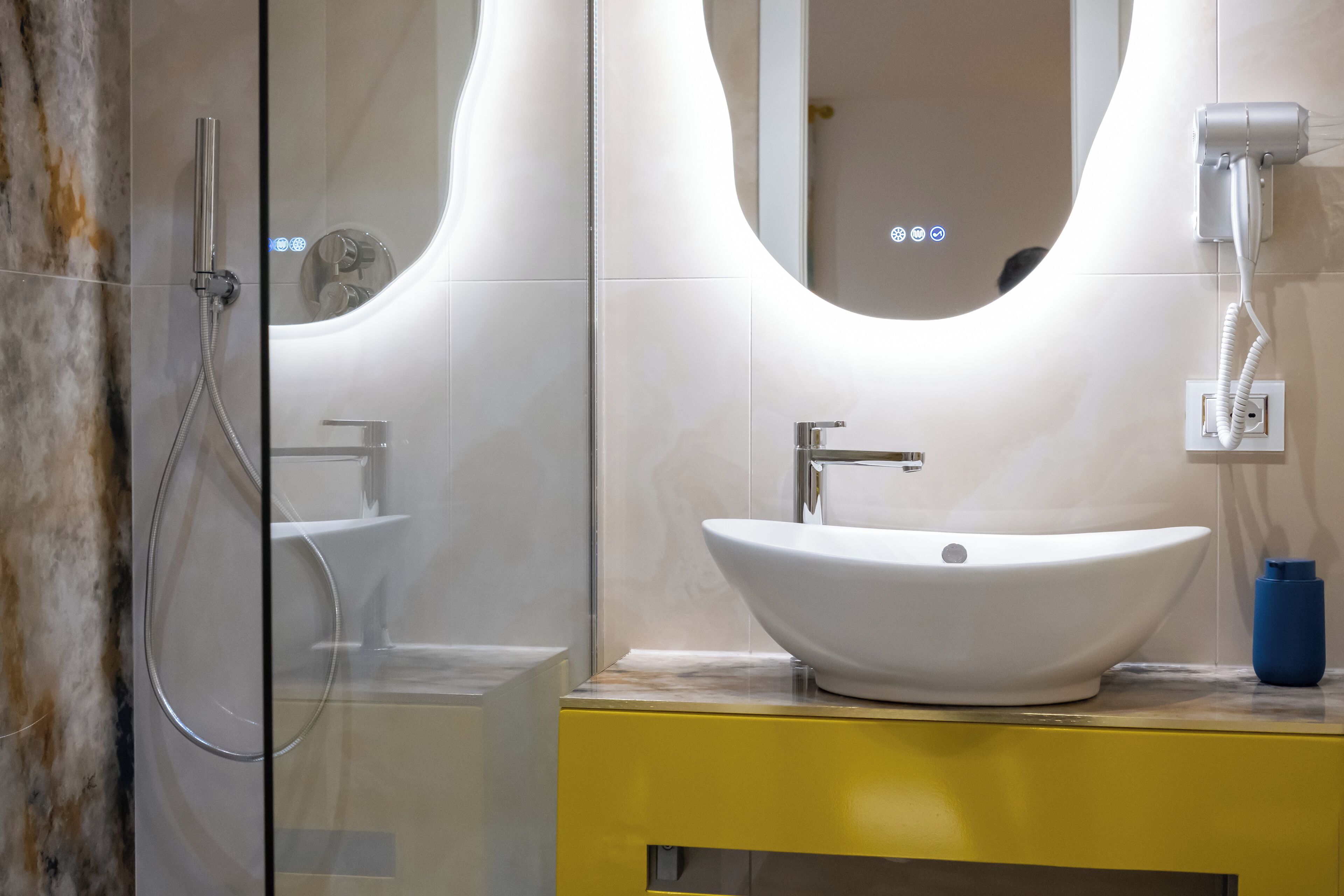 Une salle de bain moderne avec une douche à parois de verre, un lavabo sur colonne blanc et un meuble-lavabo jaune.