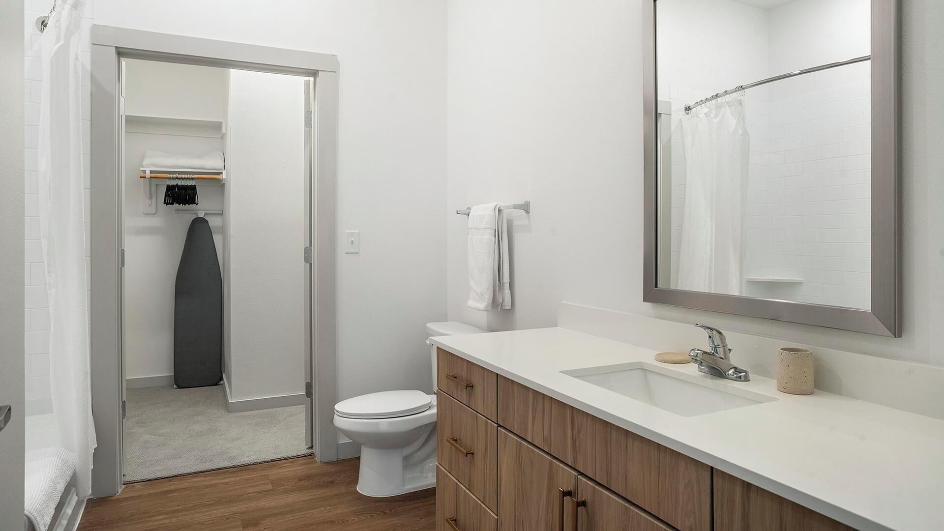 Ein modernes Badezimmer mit Toilette, Holzwaschtisch und großem Spiegel.