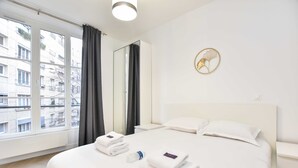 A hotel room with a large bed, two bedside tables, a mirror, and a view of the city through large windows. - Calm Apartment -1br/4p- Bastille (Paris)