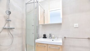 A modern bathroom with a glass shower enclosure, a white sink with a mirror above it, and wooden cabinets. - Calm Apartment -1br/4p- Bastille (Paris)