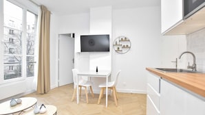A modern kitchen with white cabinetry, a wooden countertop, and a built-in oven. There is a dining area with a white table and chairs, and a TV mounted on the wall. - Calm Apartment -1br/4p- Bastille (Paris)