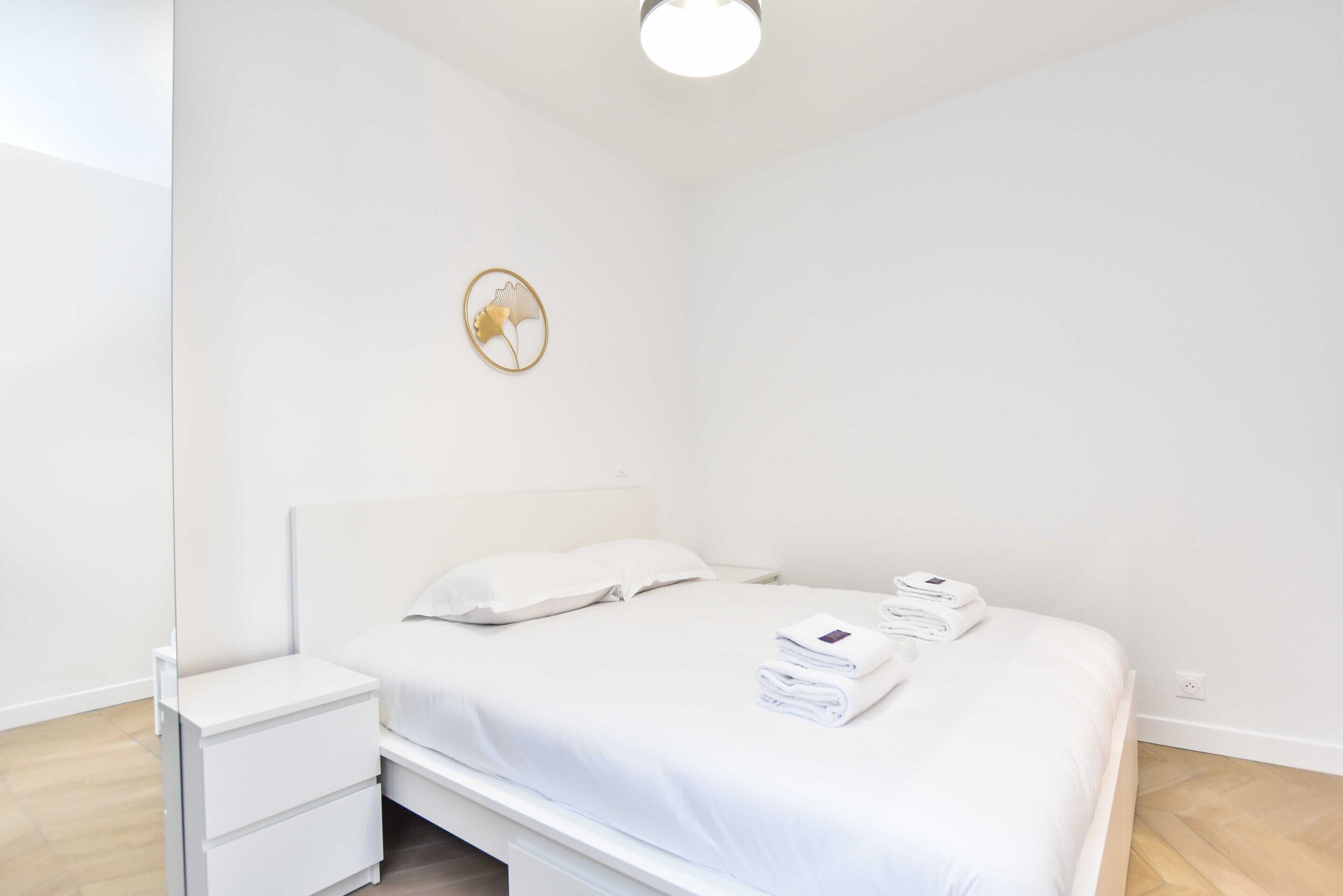 A minimalist bedroom with a bed, a nightstand, and a wall-mounted light fixture.