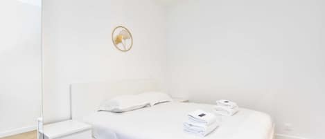 A minimalist bedroom with a bed, a nightstand, and a wall-mounted light fixture.