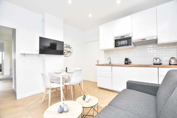 Een moderne keuken met witte kastjes, een magnetron en een koffiezetapparaat. Er is een eethoek met een witte tafel en stoelen.