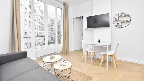 A modern living room with a sofa, a dining table with chairs, a TV mounted on the wall, and a window with curtains. - Calm Apartment -1br/4p- Bastille (Paris)