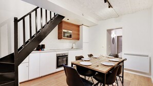 Una cocina moderna con armarios blancos, una mesa de comedor de madera dispuesta para cuatro personas y una escalera negra.