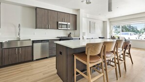 Een moderne keuken met donkerhouten kastjes, roestvrijstalen apparatuur en een centraal eiland met barstoelen.