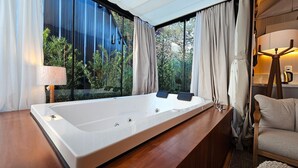 Un baño moderno con una bañera grande, un tocador de madera y vistas a la vegetación exterior.
