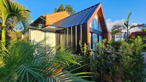 Una casa moderna con techo inclinado, ventanas amplias y rodeada de abundante vegetación.