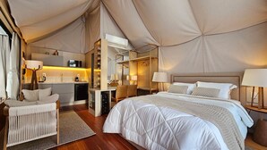 Una habitación con carpa, una cama, mesita de noche, lámpara y un área de kitchenette.