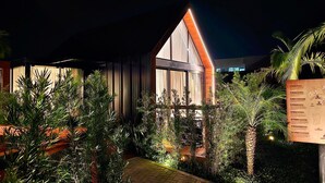Un bâtiment moderne doté de grandes fenêtres et d’un toit en pente, entouré d’une végétation luxuriante et bordé d’un chemin pavé.