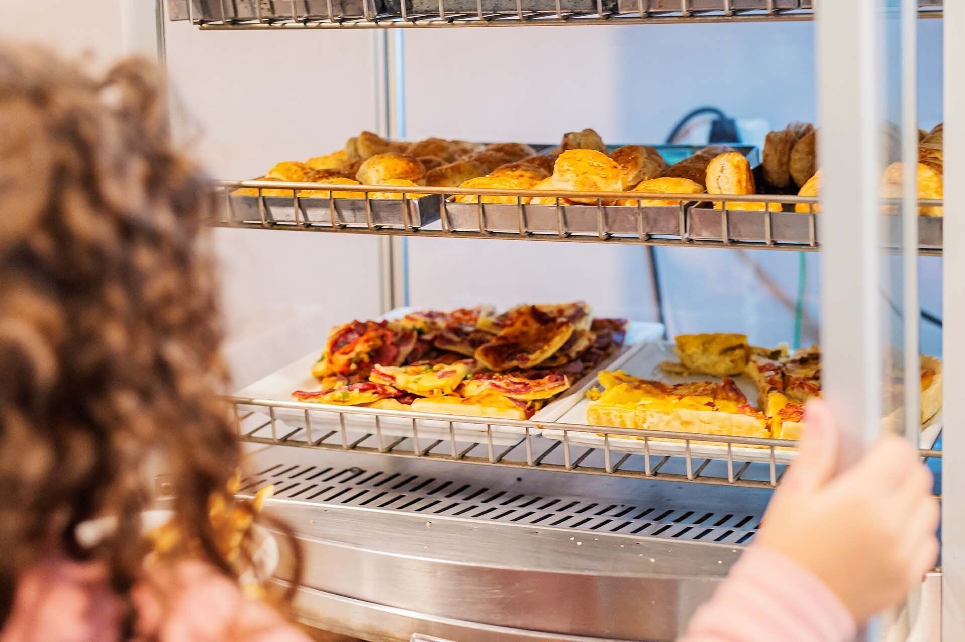 A person reaching into a multi-tiered display case containing various baked goods.