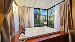 Ein Zimmer mit einer großen Badewanne, beigen Vorhängen und Blick ins Grüne.