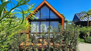 Ein modernes Haus mit einem dreieckigen Dach, großen Fenstern und üppiger, grüner Bepflanzung.