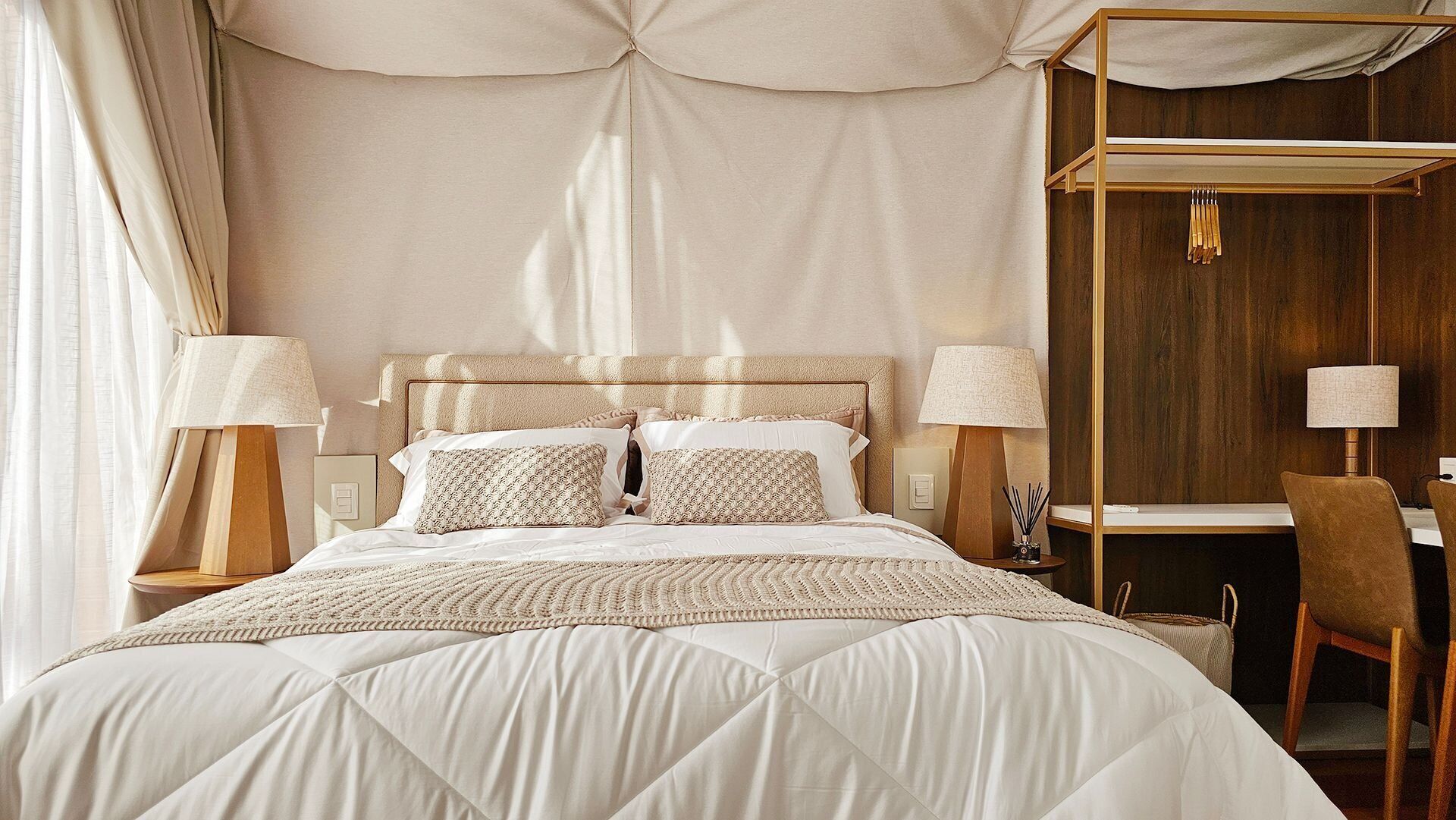 A spacious bedroom with a large bed, two bedside tables with lamps, a wooden desk, and a chair.