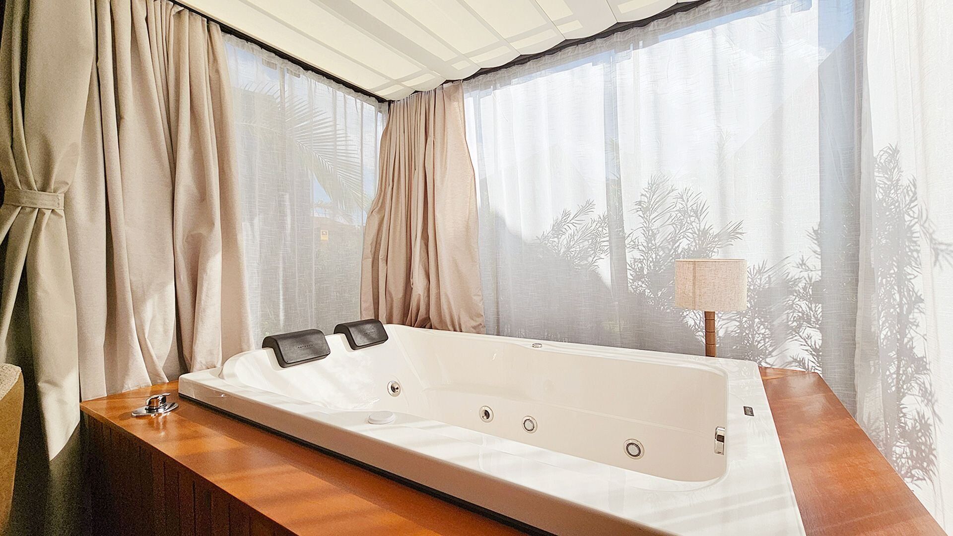 Une salle de bain moderne avec une grande baignoire, un meuble-lavabo en bois et des rideaux en voile.