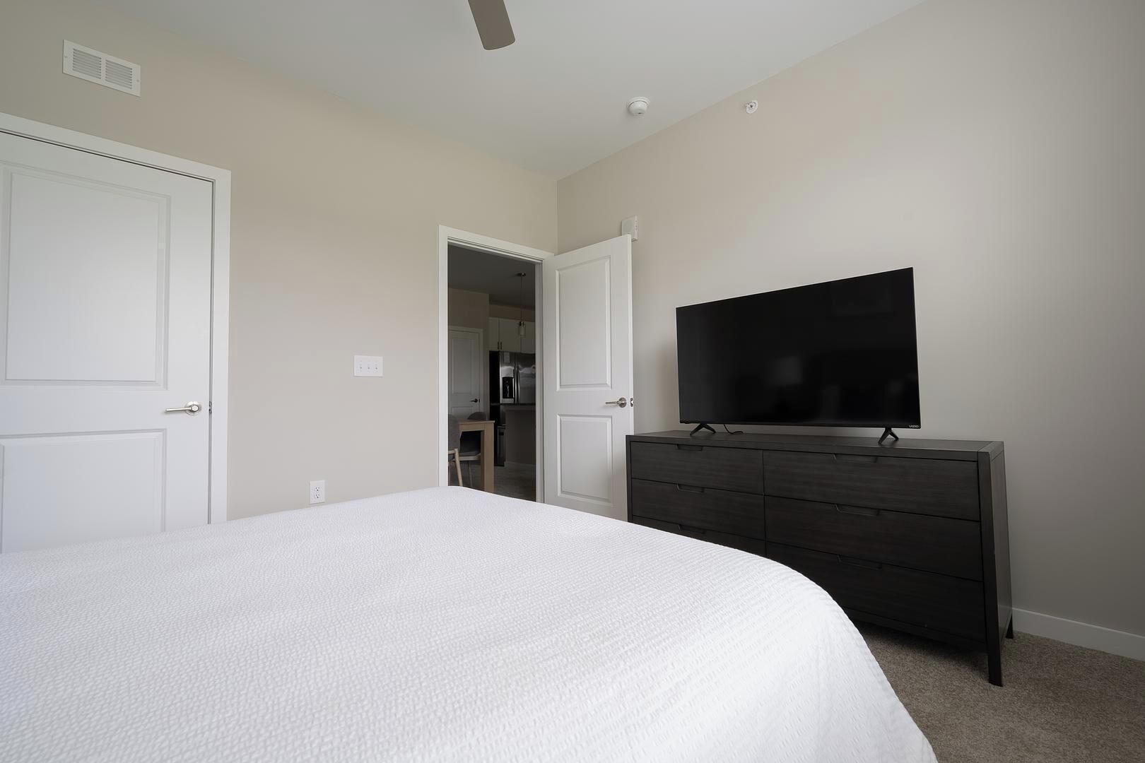 Une chambre à coucher avec un grand lit, une commode sombre, un téléviseur à écran plat et une porte donnant sur une salle de bain.