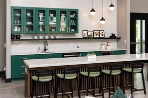 A modern kitchen with green cabinets, a white countertop, and bar stools.