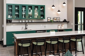 Una cucina con mobili verdi, un piano di lavoro bianco e sgabelli da bar.