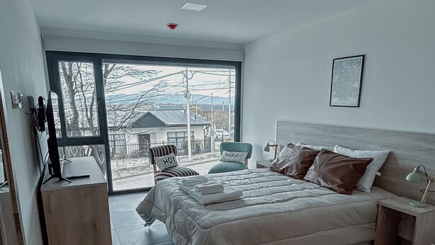 A bedroom with a large bed, a desk, and a chair. There is a window with a view of the outside. - Gente del Sur - Buena Vista (Ushuaia)