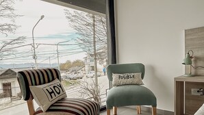 A modern bedroom with a large window, a striped chair with a pillow, a green chair, and a bedside table with a lamp. - Gente del Sur - Buena Vista (Ushuaia)