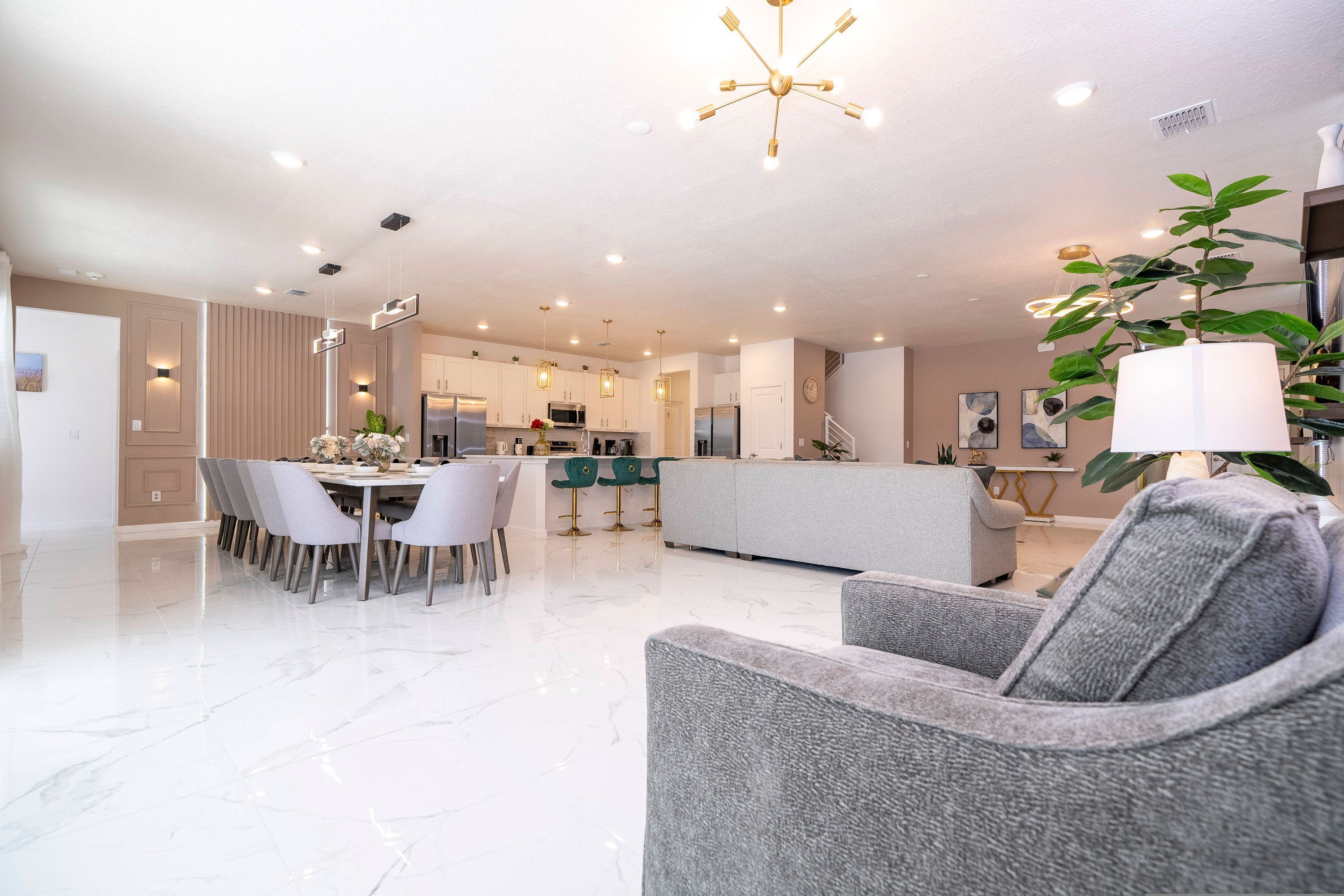 A spacious living area with a dining table, grey sofas, and a kitchen in the background.