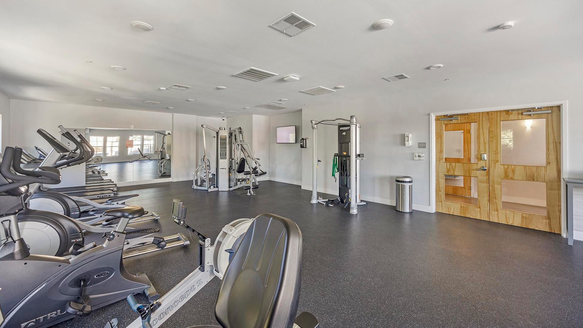 A gym with treadmills, weight machines, and a mirror wall.