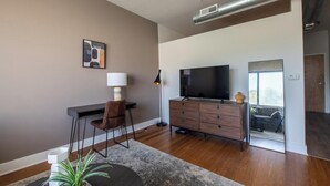 Una sala de estar moderna con una televisión de pantalla plana, un mueble de madera, un escritorio con una silla y un ventanal grande.