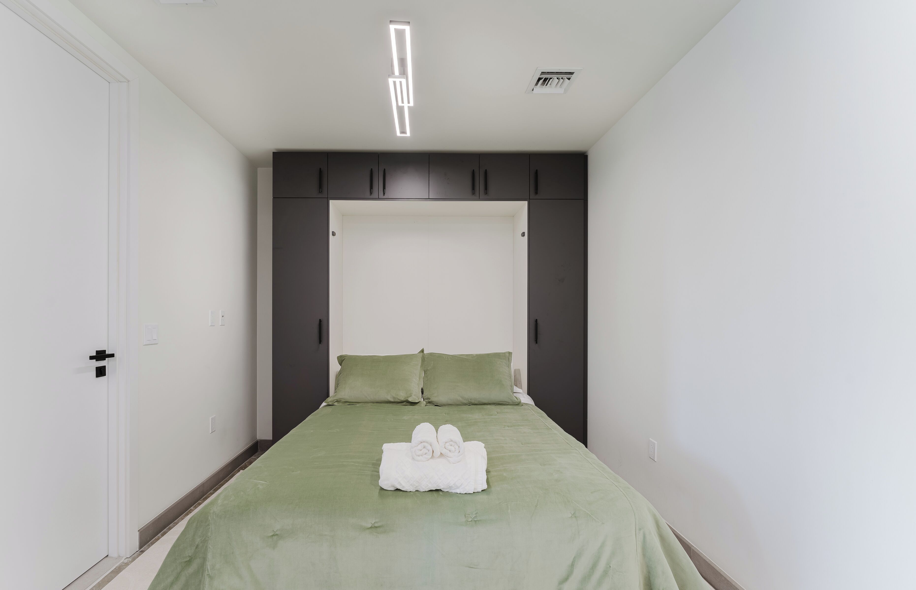 A bedroom with a bed, green bedding, and a white towel on the bed.